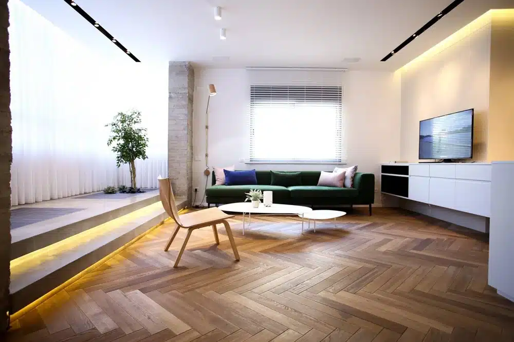 A living room with a herringbone pattern wooden floor and a two-step concrete platform with built-in lighting.