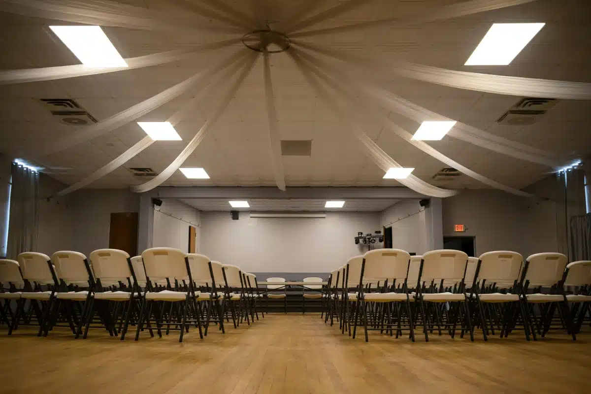 Empty folding chairs on a polished wooden floor facing a stage.